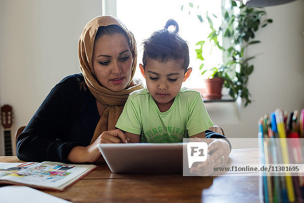 Mutter unterstützt den Sohn bei der Verwendung des digitalen Tabletts während des Studiums zu Hause.