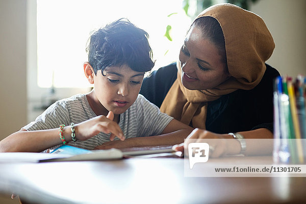 Lächelnde Mutter unterstützt den Sohn bei der Benutzung des digitalen Tabletts während des Studiums zu Hause.