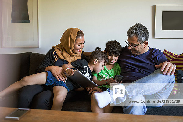 Playful family using smart phone while sitting on sofa at home