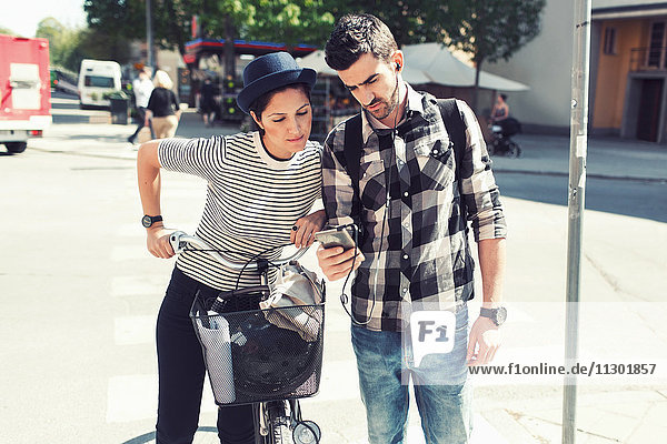 Couple using smart phone while standing with bicycle on street