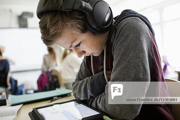 Seitenansicht des Jungen  der Kopfhörer hört  während er ein digitales Tablett im Klassenzimmer benutzt.