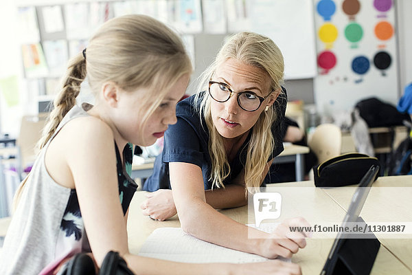 Teacher helping schoolgirl with digital tablet in classroom