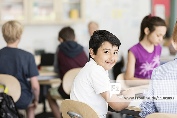 Portrait of happy boy sitting with students in classroom
