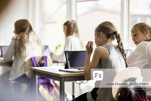 Rear view of girls sitting on desk in classroom