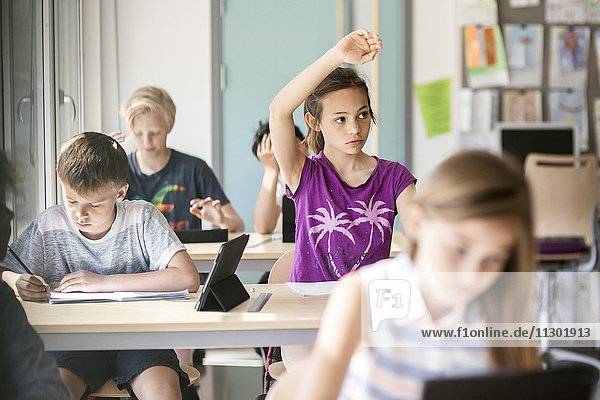 Schülerin hebt Hand am Schreibtisch im Klassenzimmer
