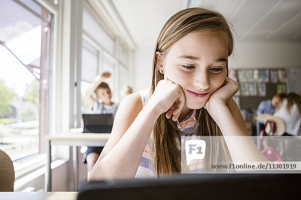 Schülerin liest vom digitalen Tablett am Schreibtisch im Klassenzimmer