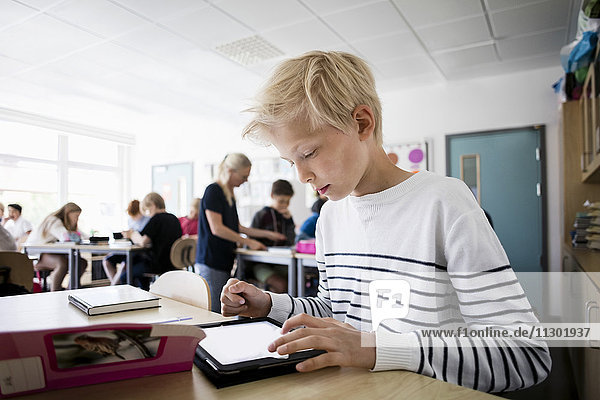 Junge mit Tablet PC am Schreibtisch im Klassenzimmer