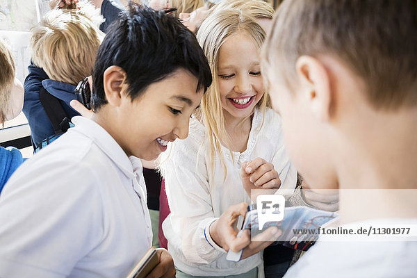 Happy school kids using mobile phone in corridor