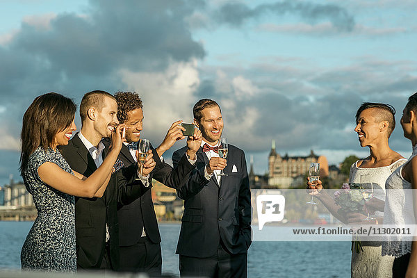Glücklicher Mann mit Freunden beim Fotografieren eines lesbischen Paares bei der Hochzeit