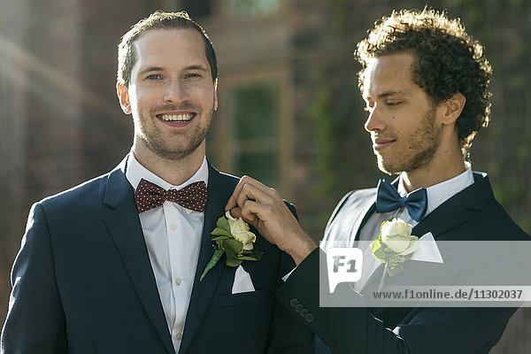 Portrait of happy man standing with gay partner adjusting boutonniere