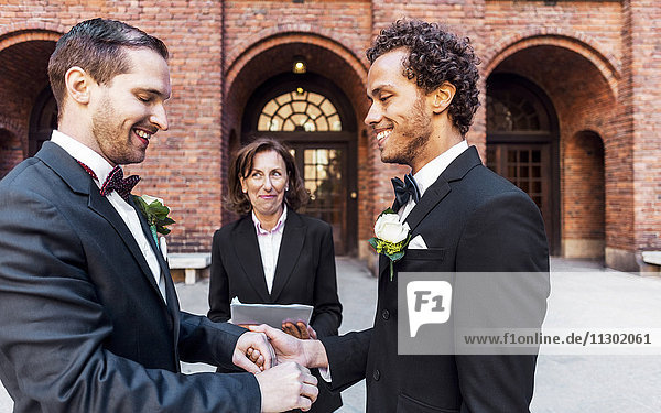 Priester sieht den Mann an  der die Hand des schwulen Partners während der Hochzeitszeremonie hält.