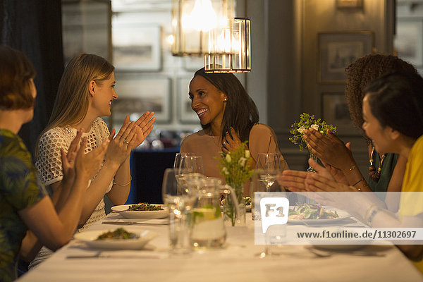 Smiling women friends dining and celebrating clapping at restaurant table