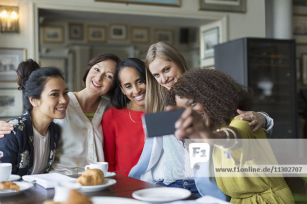 Smiling women friends taking selfie at restaurant table