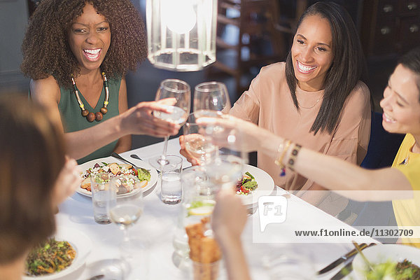 Smiling women friends toasting white wine glasses dining at restaurant table