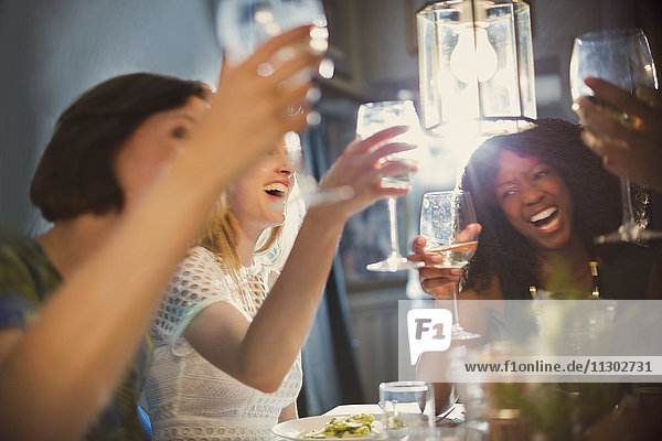 Laughing women friends toasting white wine glasses dining in restaurant