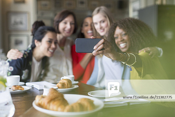 Lächelnde Frauenfreunde nehmen Selfie mit Fotohandy im Restaurant mit