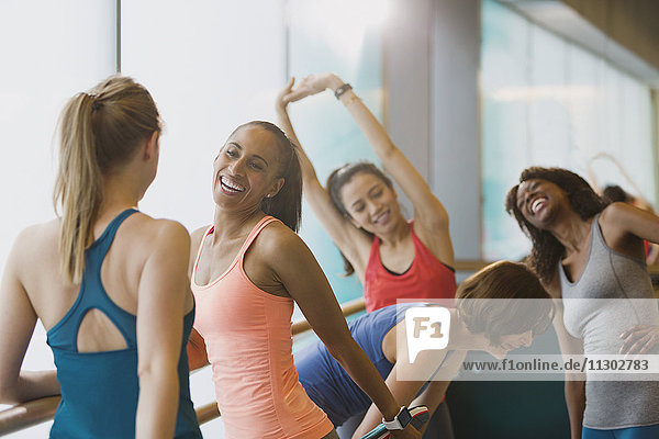 Smiling women talking and stretching in exercise class gym studio