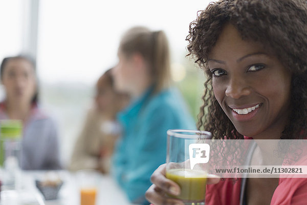 Portrait lächelnde Frau trinkt gesunden grünen Smoothie im Café mit Freunden