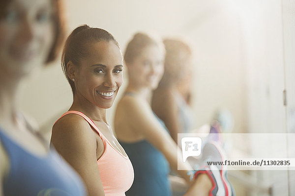 Portrait lächelnde Frauen  die ihre Beine an der Stange im Fitnessstudio ausstrecken.