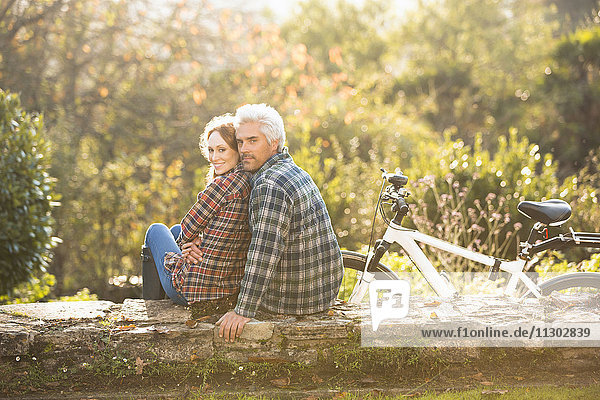 Portrait affectionate couple with bicycle resting on stone wall in autumn park