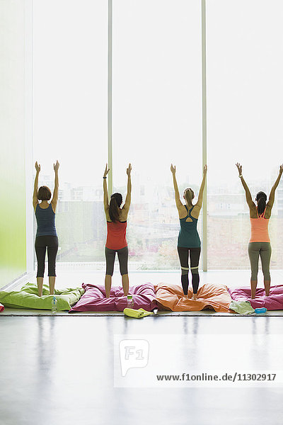 Frauen auf Kissen  die sich mit erhobenen Armen im Fitnessstudio der Übungsklasse strecken.