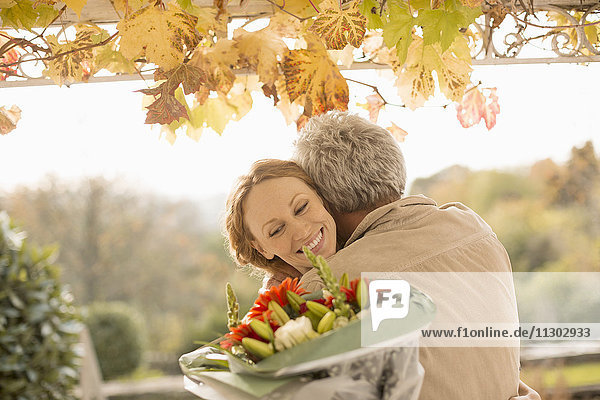 Ehemann überrascht Frau mit Blumenstrauß auf Herbstterrasse