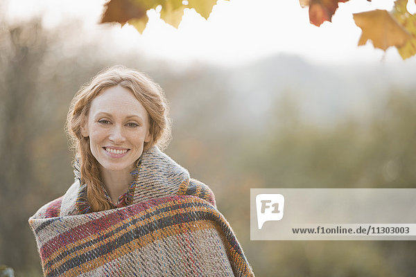 Portrait smiling woman wrapped in blanket in autumn park