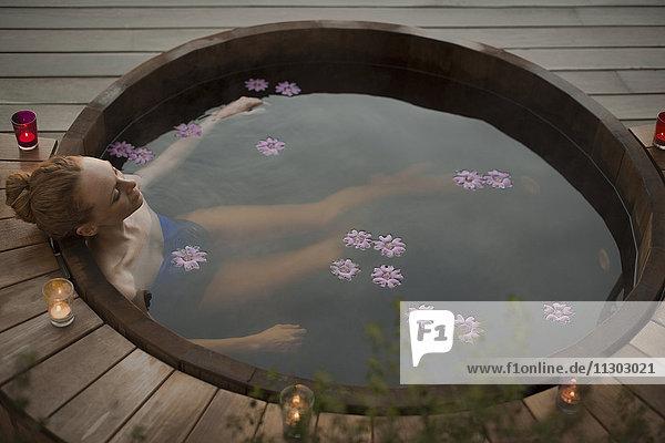 Gelassene Frau  die im Whirlpool mit Blumen und Kerzen auf der Terrasse badet