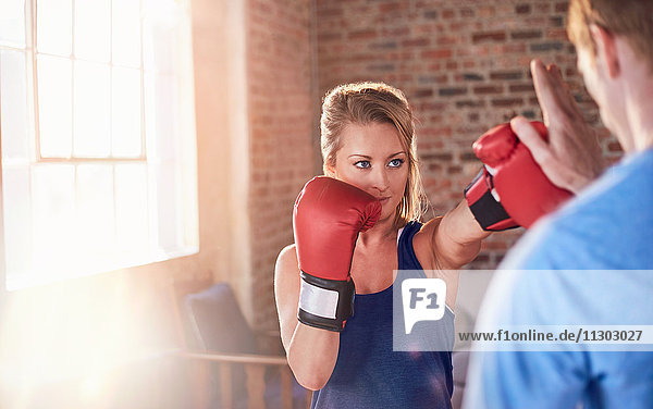 Young female boxer practicing boxing with trainer in gym studio