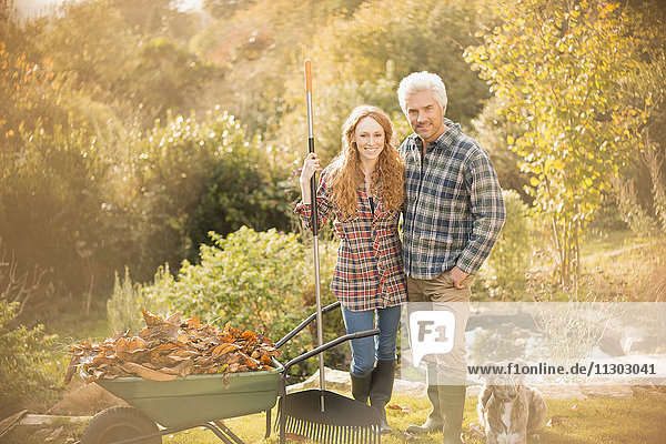 Portrait lächelndes Paar mit Hund bei der Gartenarbeit Laubharken im Herbstgarten