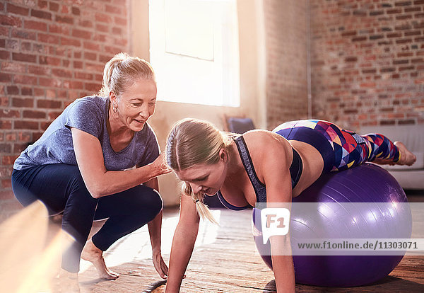 Fitnesstrainerin hilft der jungen Frau beim Balancieren auf dem Fitnessball im Studio.