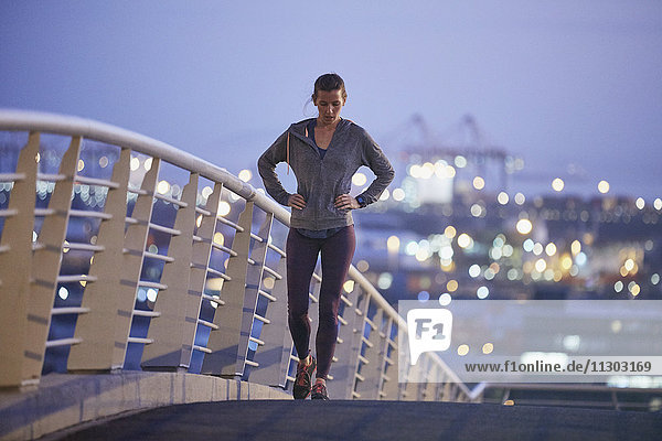 Läuferin ruht sich aus und streckt die Beine auf einer städtischen Fußgängerbrücke in der Morgendämmerung