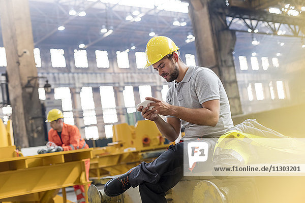 Stahlarbeiter texten mit Handy bei einer Pause in der Fabrik