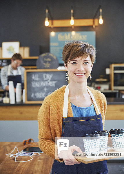 Porträt einer selbstbewussten Café-Besitzerin  die ein Tablett mit Kaffeetassen hält