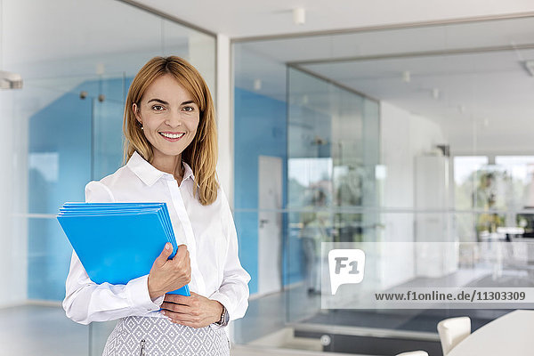 Portrait smiling businesswoman holding folders in conference room
