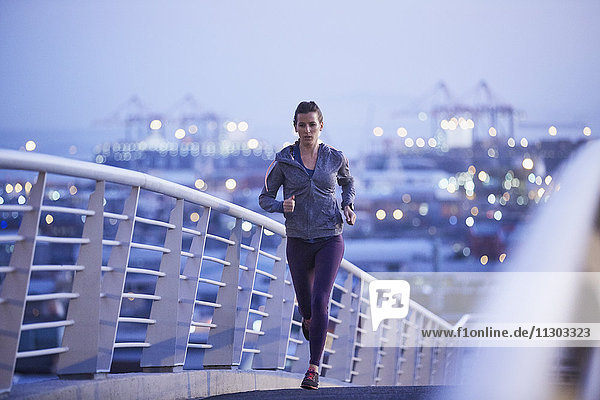 Female runner running on urban footbridge at dawn
