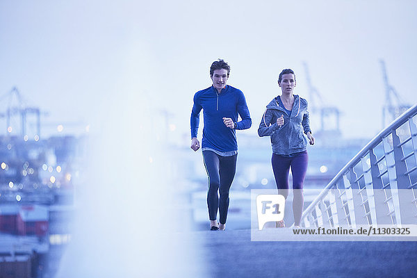 Läuferpaar beim Laufen auf einer Fußgängerbrücke in der Morgendämmerung