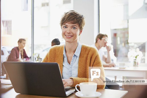 Portrait smiling businesswoman drinking coffee working at laptop in cafe