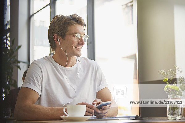 Smiling man with headphones and mp3 player listening to music drinking coffee in cafe