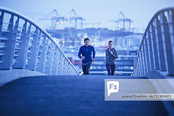 Läuferpaar beim Laufen auf einer Fußgängerbrücke in der Morgendämmerung