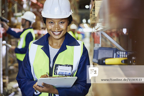 Porträt einer lächelnden Arbeiterin mit Klemmbrett in einem Vertriebslager
