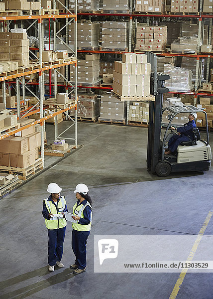 Forklift and workers meeting in distribution warehouse