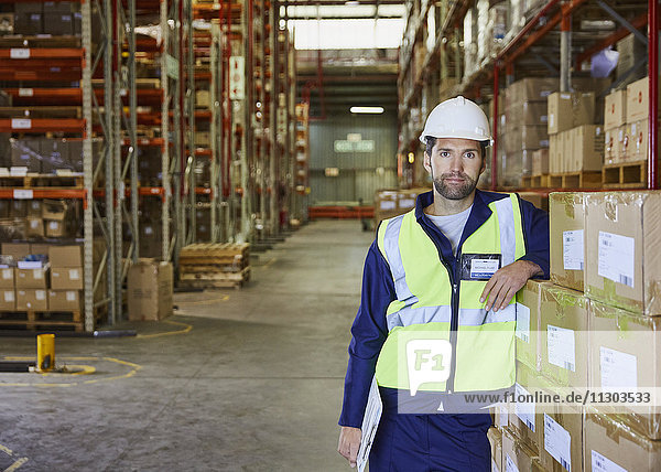 Porträt eines selbstbewussten Arbeiters  der sich auf gestapelte Kisten in einem Vertriebslager stützt