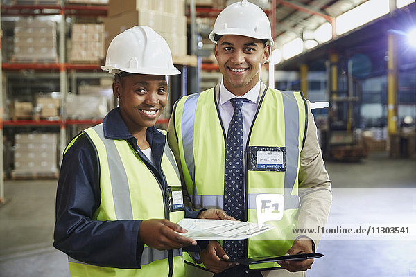 Porträt eines lächelnden Managers und eines Arbeiters mit Papierkram in einem Vertriebslager
