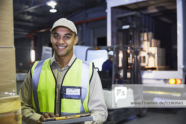 Porträt eines lächelnden Arbeiters vor einem Gabelstapler und einem Lastwagen an der Laderampe eines Vertriebslagers