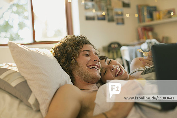 Lächelndes junges Paar liegt im Bett und benutzt einen Laptop