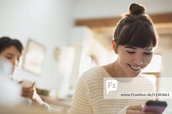 Lächelnde junge Frau  die eine SMS mit ihrem Handy schreibt