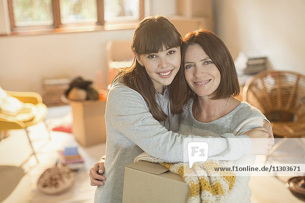 Porträt einer lächelnden Mutter  die ihrer jungen erwachsenen Tochter beim Einzug in eine neue Wohnung hilft