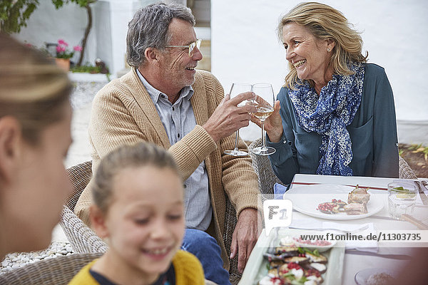 Glückliches älteres Paar stößt beim Mittagessen im Innenhof mit Weißweingläsern an