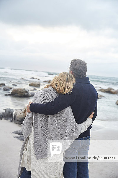 Serene affectionate couple hugging on winter beach looking at ocean